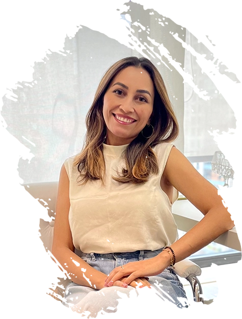 Antônia Honorato, sorrindo, de camisa sem manga bege e calça jeans, sentada em um sofá, com as mãos no colo